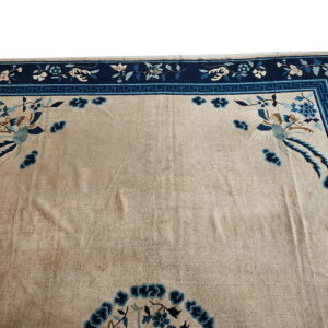 Beige rug featuring complex blue floral borders, a Greek key pattern, and central stylized bird motifs.