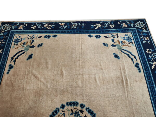 Beige rug featuring complex blue floral borders, a greek key pattern, and central stylized bird motifs.