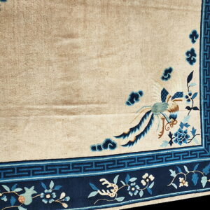 Beige rug corner with a navy blue border featuring fretwork, floral vines, and a stylized blue bird.