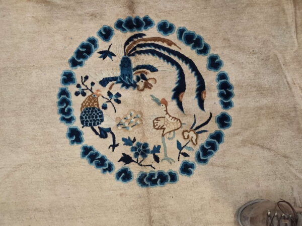 A light beige rug features a central blue and brown medallion depicting detailed birds and stylized floral motifs.