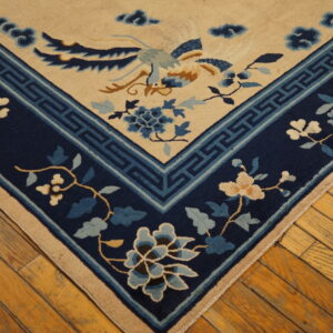 Tan rug corner with blue phoenix and floral designs, detailed navy border, resting on shiny hardwood planks.