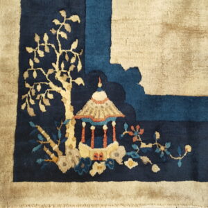 Navy rug corner with beige border, featuring a detailed scenic pattern of a pagoda and flowering foliage.