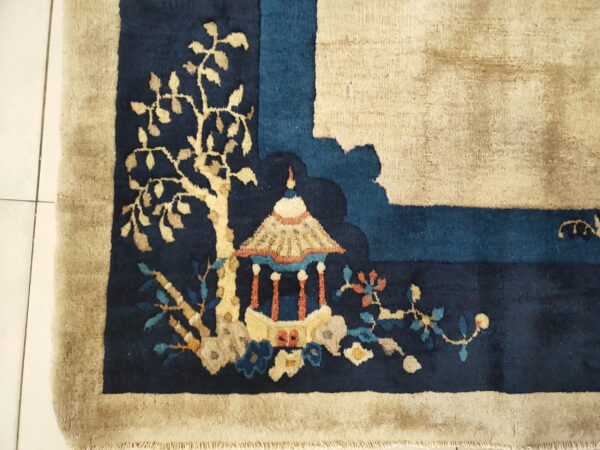 Navy rug corner with beige border, featuring a detailed scenic pattern of a pagoda and flowering foliage.
