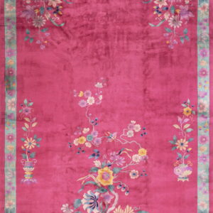 Deep pink rug with a velvety texture, featuring colorful floral sprays and a wide aqua-green scalloped border.