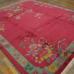 A large magenta rug with pastel floral patterns and a green border is placed on distressed wood planks.