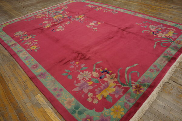 A large magenta rug with pastel floral patterns and a green border is placed on distressed wood planks.