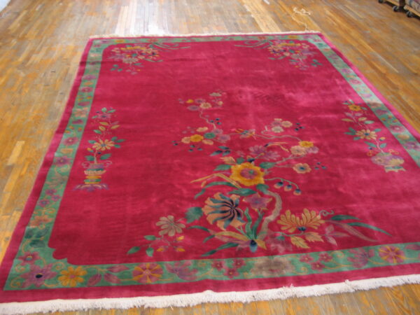 Fuchsia rug with colorful floral sprays and a wide sage green border on light plank wood floors.
