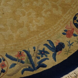 A curved beige rug section showing tone-on-tone texture, navy border, colorful blue and pink floral accents, and fringe.