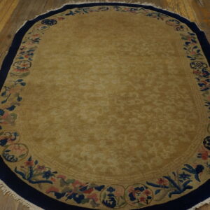 Gold oval rug with deep navy and floral borders lying on distressed wooden plank flooring.