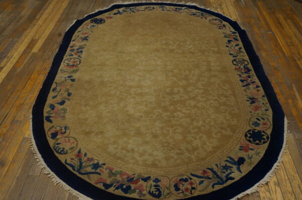 Gold oval rug with deep navy and floral borders lying on distressed wooden plank flooring.