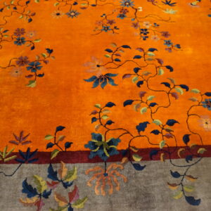 Plush rug featuring a vibrant orange field and gray border with a multicolor winding floral vine pattern.