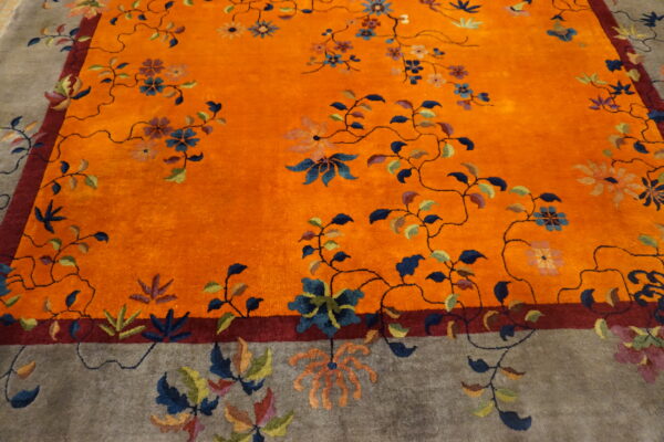 Plush rug featuring a vibrant orange field and gray border with a multicolor winding floral vine pattern.