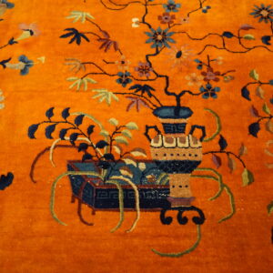 Orange high-pile rug detail showing a decorative vase and vines with blue, green, and multicolored flowers.