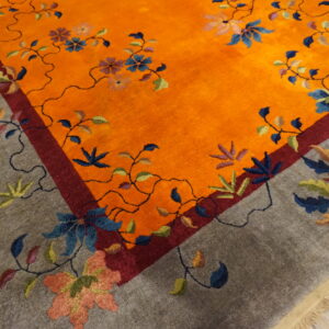 Vibrant orange and gray rug with a winding botanical pattern on wooden floorboards.