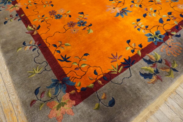 Vibrant orange and gray rug with a winding botanical pattern on wooden floorboards.