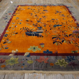 Saffron orange rug featuring a large multicolored floral vase design and a gray pictorial border on wood floor.