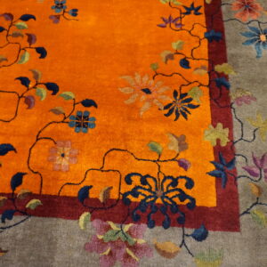 Detail view showing a vibrant orange field and taupe border accented with multicolored flowers and vines.