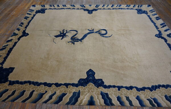 Beige rug with a central blue dragon motif and a decorative blue and tan border on wood planks.