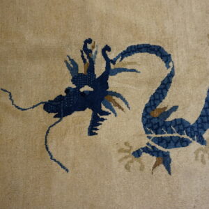 Beige low-pile rug detail showing a navy blue dragon pattern with golden-tan elements.