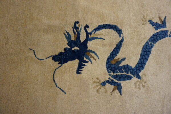 Beige low-pile rug detail showing a navy blue dragon pattern with golden-tan elements.