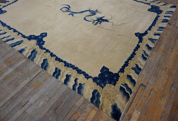 Beige rug with a blue dragon and cloud-pattern border rests on worn wide plank wood flooring.