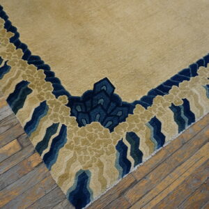 Carved beige rug with a stylized blue and green border lying on distressed hardwood flooring.