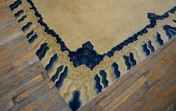 Carved beige rug with a stylized blue and green border lying on distressed hardwood flooring.