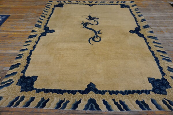 Tan area rug with a dark blue stylized dragon and wave-like cloud border over plank flooring.
