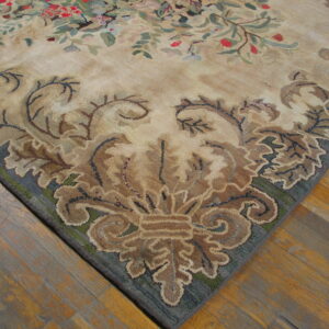 Close-up of a hooked rug corner featuring a beige field and dark blue border with elaborate brown scrollwork on wood floors.