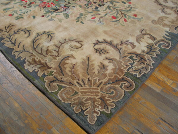 Close-up of a hooked rug corner featuring a beige field and dark blue border with elaborate brown scrollwork on wood floors.