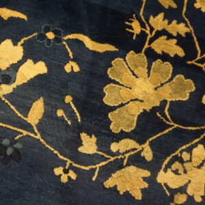 Plush navy blue rug surface with large scrolling floral and vine patterns in gold and khaki.