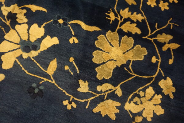 Plush navy blue rug surface with large scrolling floral and vine patterns in gold and khaki.