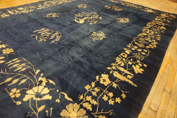 Navy blue rug featuring a vibrant gold floral border and scattered patterns on light wood flooring.
