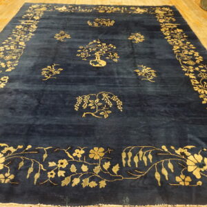 A deep indigo rug with gold floral borders and scattered motifs lies on light hardwood floors.