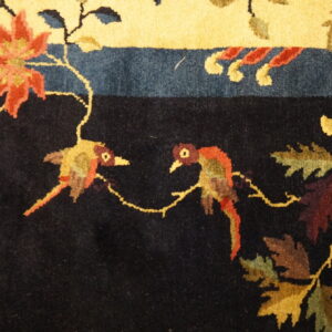 Black field rug featuring two colorful birds, autumn foliage, and red florals near a bright yellow border.