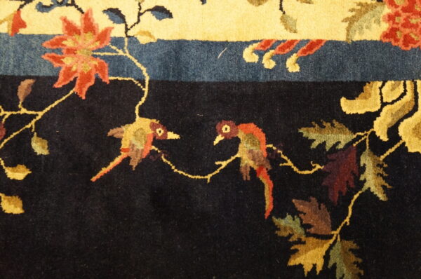 Black field rug featuring two colorful birds, autumn foliage, and red florals near a bright yellow border.