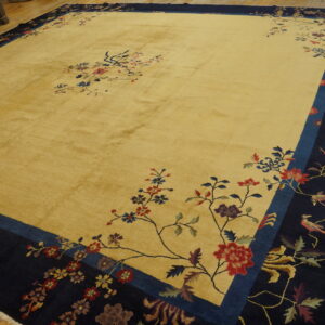 Large golden-yellow rug with a dark navy border, colorful floral branches, and birds on hardwood.