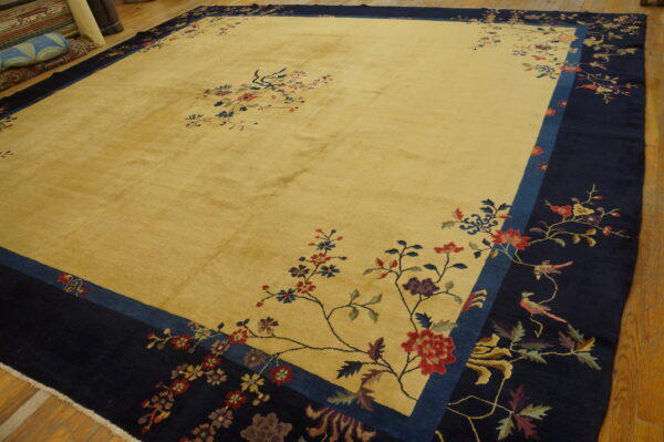 Large golden-yellow rug with a dark navy border, colorful floral branches, and birds on hardwood.
