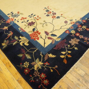Navy and cream rug with a colorful floral and bird motif rests on worn wood planks.