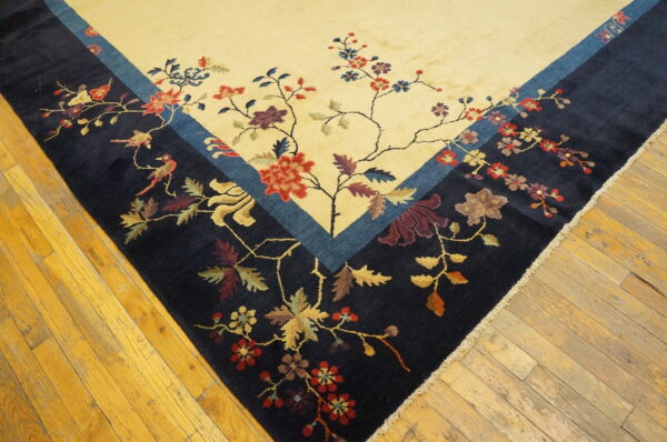 Navy and cream rug with a colorful floral and bird motif rests on worn wood planks.