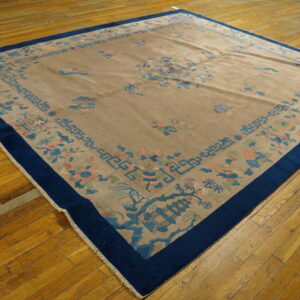 Tan rug featuring blue and pink motifs, a navy border, placed on worn wood floors.