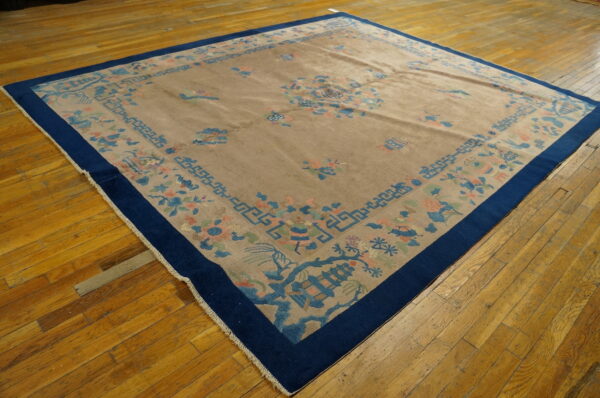 Tan rug featuring blue and pink motifs, a navy border, placed on worn wood floors.