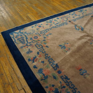 High-pile tan rug with a blue and coral floral border rests partially on worn wood flooring.