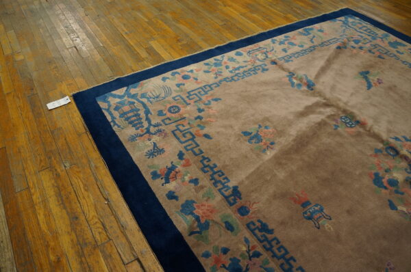 High-pile tan rug with a blue and coral floral border rests partially on worn wood flooring.