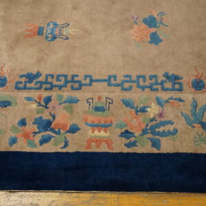 Tan rug border featuring blue geometric fretwork, coral floral motifs, and a solid navy edge on a wood floor.