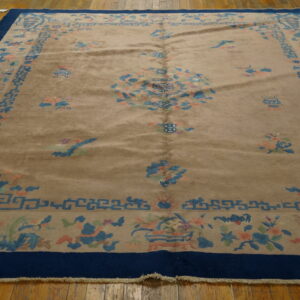 Tan high pile rug with a dark blue border and subtle floral motifs rests on honey-colored wood floors.