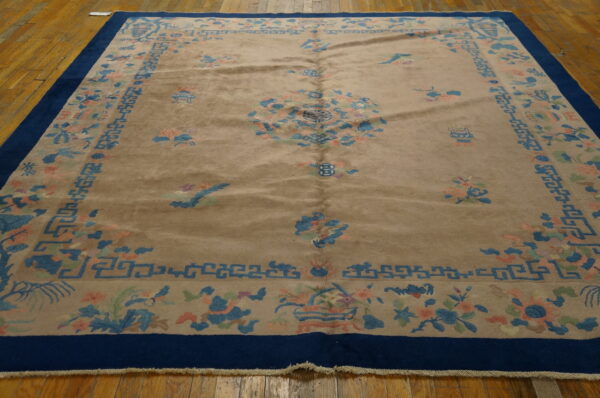 Tan high pile rug with a dark blue border and subtle floral motifs rests on honey-colored wood floors.