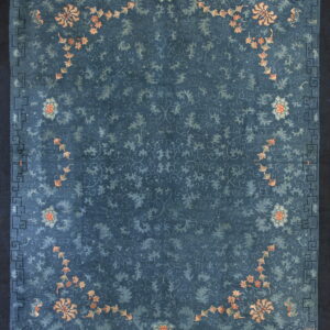 Dark blue rug with faded blue floral scrolling, peach flowers, and a dark geometric key border.