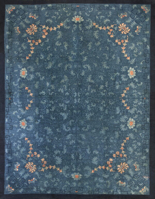 Dark blue rug with faded blue floral scrolling, peach flowers, and a dark geometric key border.