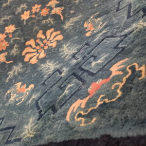 Blue-green rug with scattered peach florals and dark blue geometric line patterns.